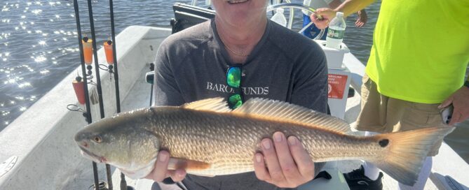 A male angler holding a large red drum in a skiff on the water around Topsail Island.