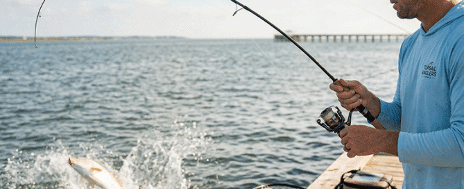 Angler on a dock carefully fighting a jumping redfish using light spinning tackle and a properly set drag.