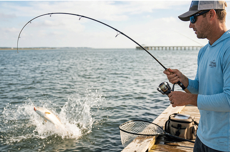 Angler on a dock carefully fighting a jumping redfish using light spinning tackle and a properly set drag.